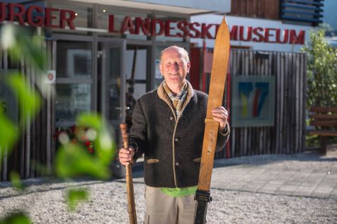 Elderly man with antique ski equipment stands in front of the Ski Museum Werfenweng.