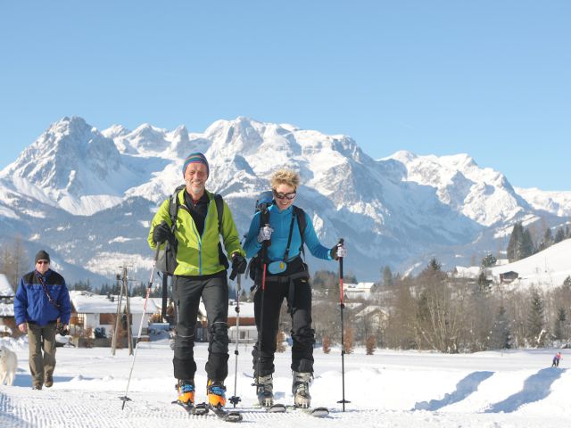 2 snowshoe hikers. In the background you can see the Tennengebirge and a walker with a dog.
