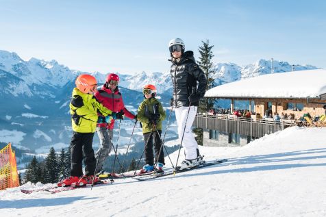 2 adults and 2 children stand together in ski equipment. In the background you can see a restaurant.